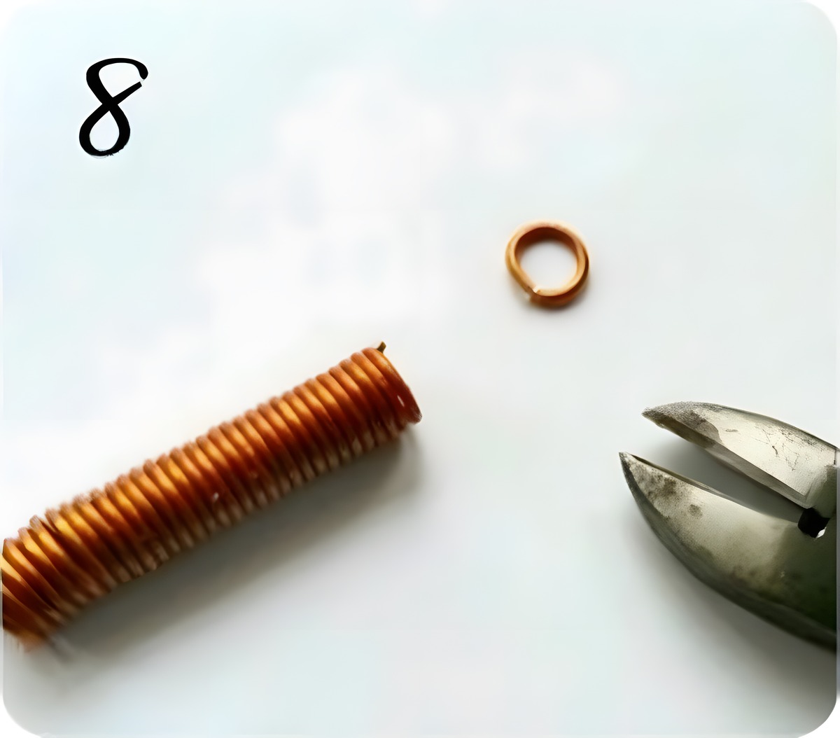 A single finished copper jump ring lying next to cutting pliers after being cut from the coil