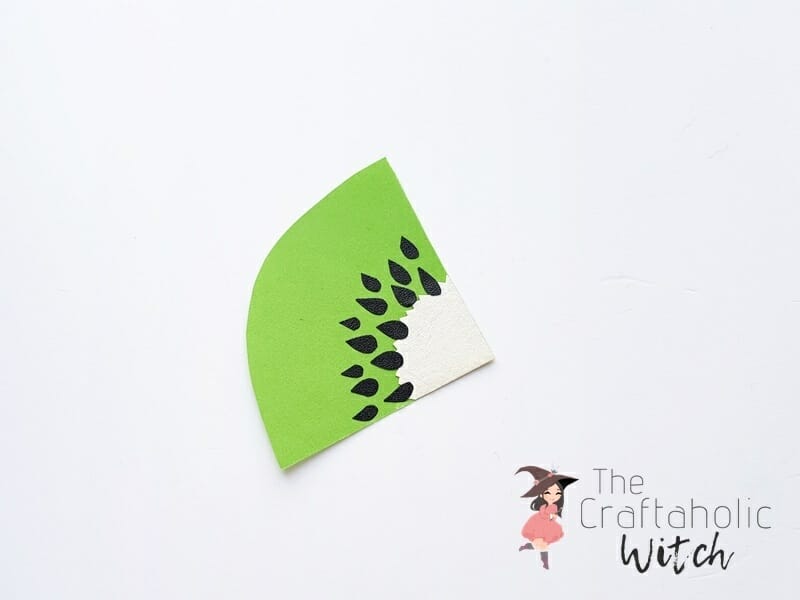 Kiwi bookmark step 3, adding the seeds Attaching black paper teardrop seeds onto the green and white kiwi slice cutout
