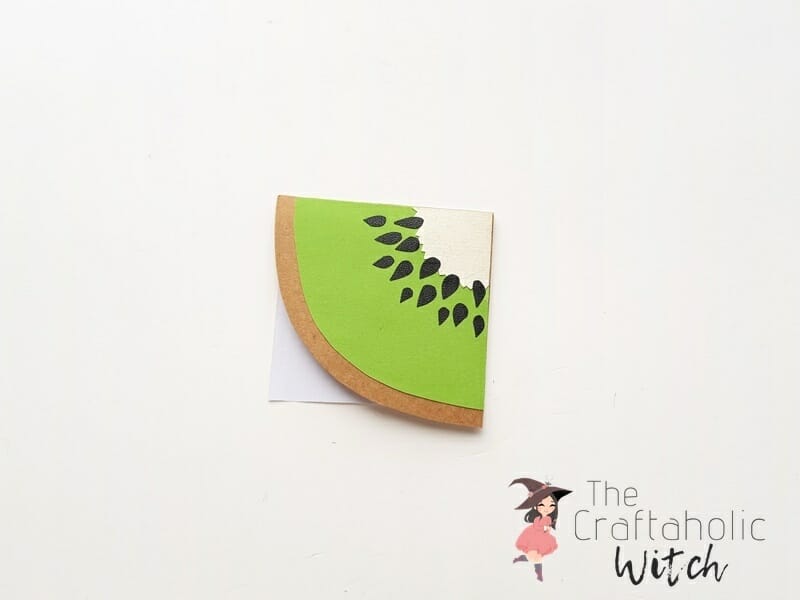 Kiwi bookmark step 5, attaching to the bookmark corner Attaching the finished paper kiwi slice to the corner of a folded origami bookmark