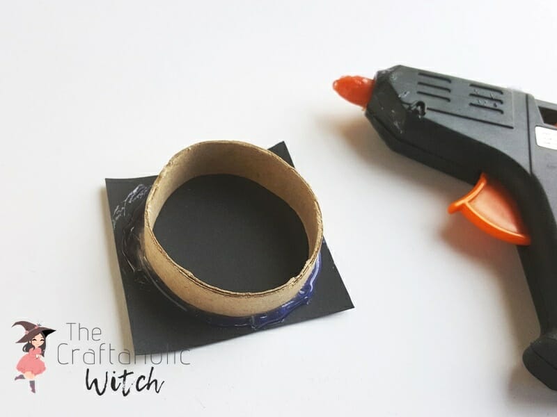 Gluing a toilet paper roll ring onto a black cardstock square to seal the wire picture holder mold