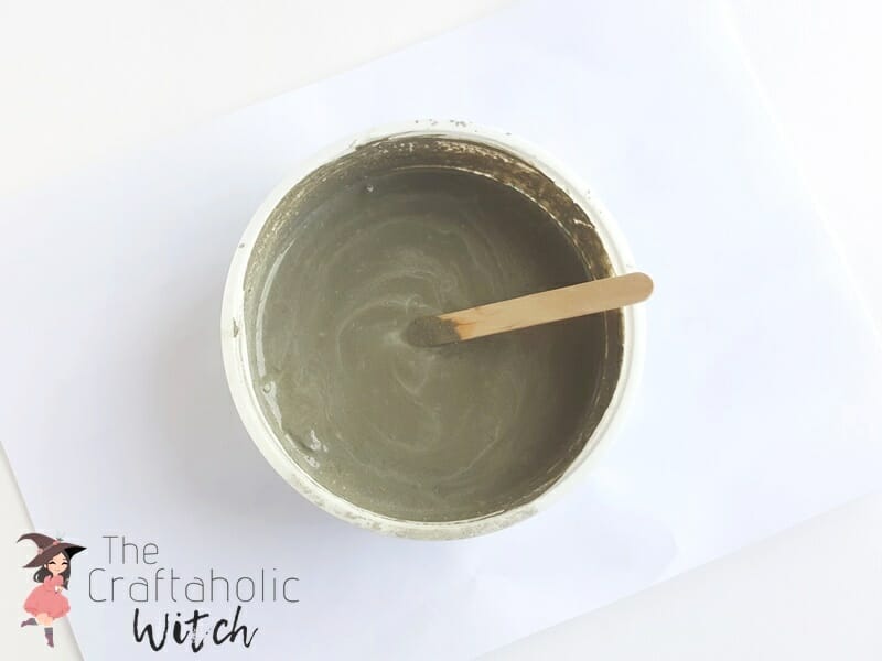 Thick concrete mixture in a small tub, stirred with a wooden stick, for a wire picture holder base