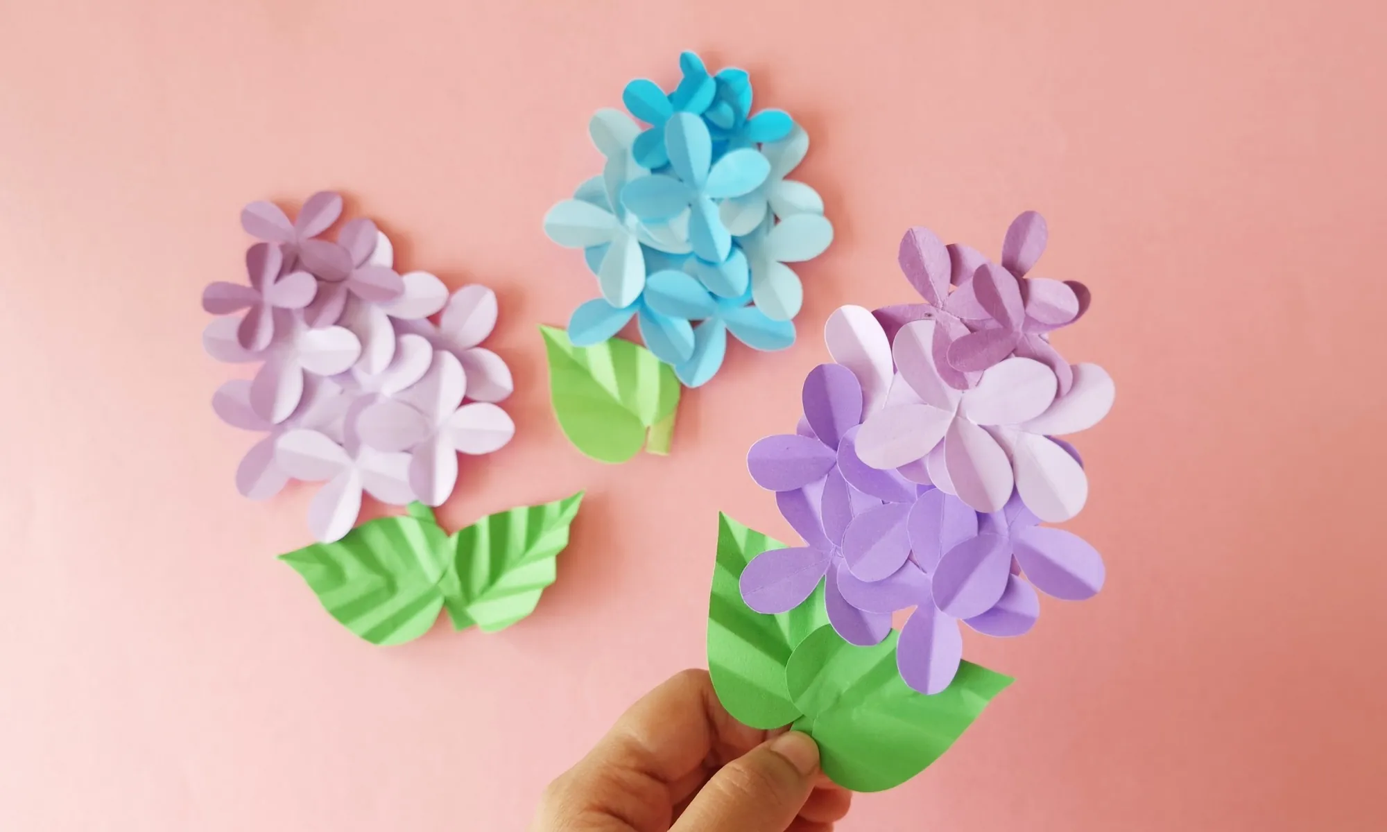 Paper lilac flower craft cover image Finished paper lilac flowers in pastel purple and blue shades with folded green leaves