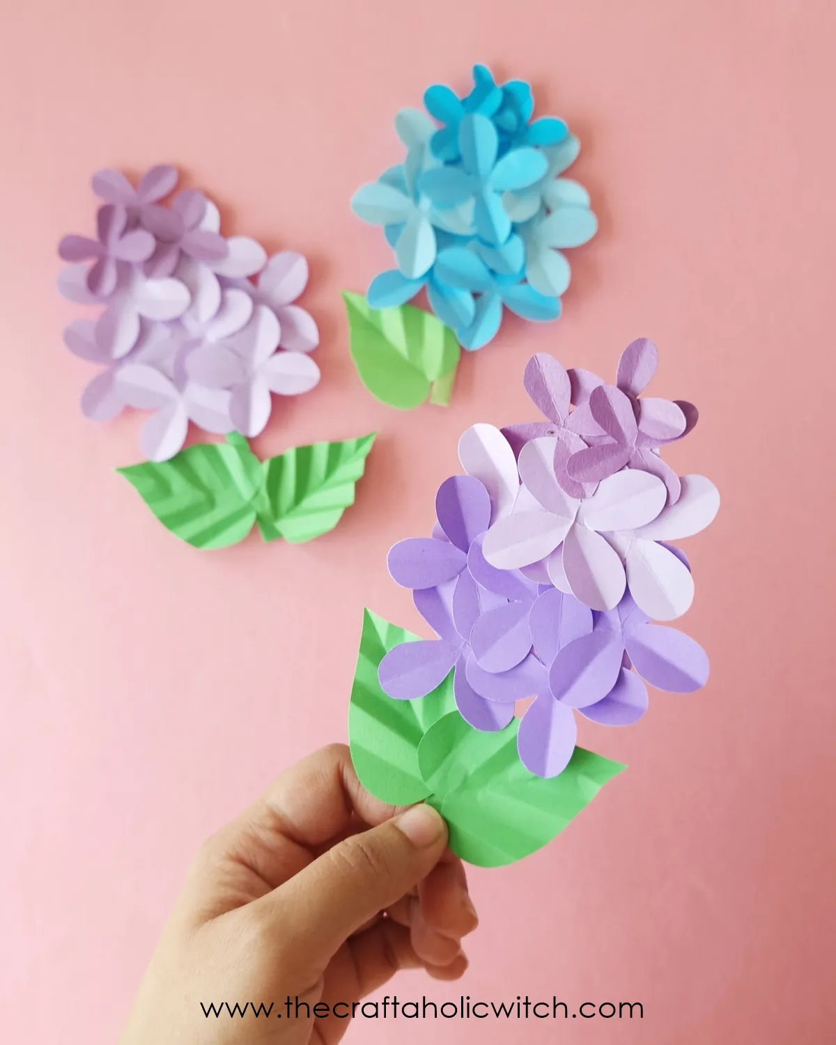 Paper lilac flower craft long image 2 Hand holding a finished paper lilac flower with layered purple petals