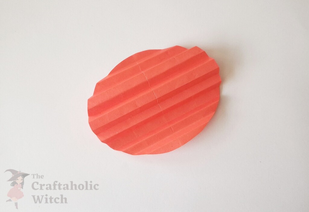 Pink paper circle with multiple radiating crease lines from center showing accordion fold guidelines for 3D paper heart