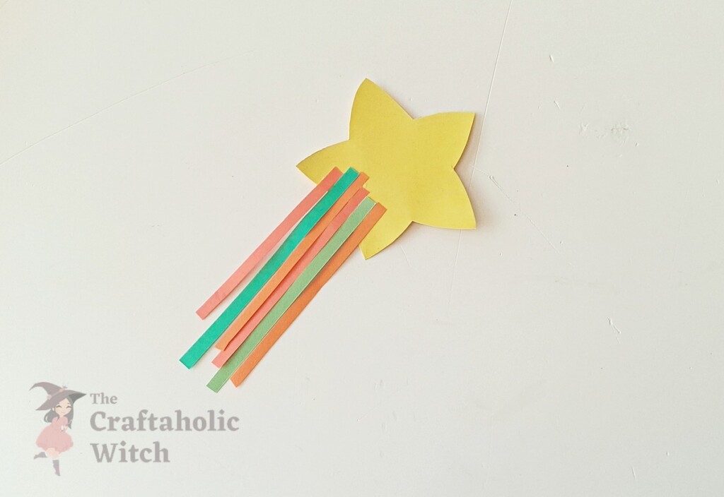 "Multiple colorful paper strips attached to star creating rainbow wand effect for pencil topper