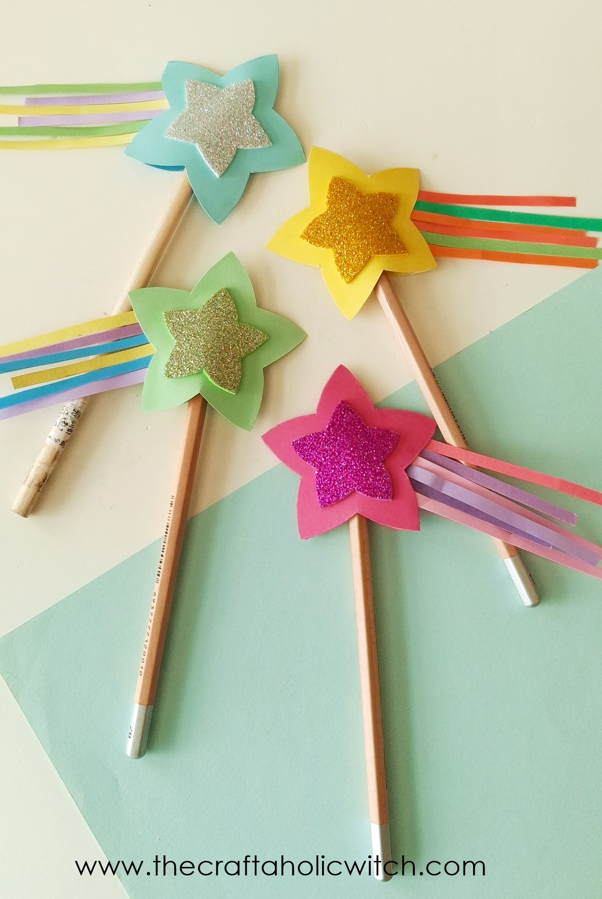 Four colorful DIY paper star pencil toppers with glitter centers and paper streamer tails.