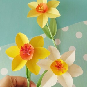 Three completed paper daffodil flowers in yellow and cream displayed in a small vase