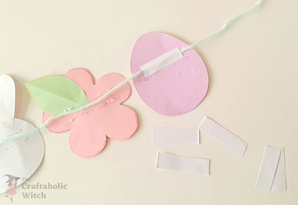 Small paper strip being glued over the yarn on the back of one garland piece