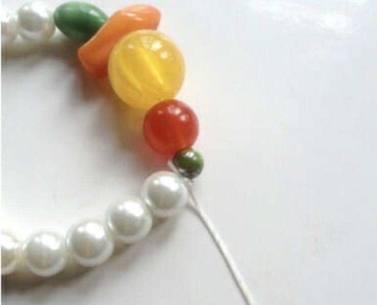 Stringing colorful accent beads onto elastic thread for a mixed beaded bracelet