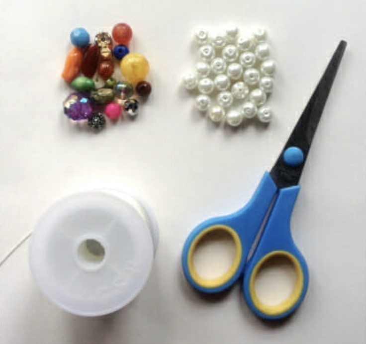 Supplies for a mixed beaded bracelet including faux pearls, colorful accent beads, elastic thread, and scissors