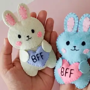 Two finished felt bunny plush toys, one cream and one blue, each holding a BFF heart