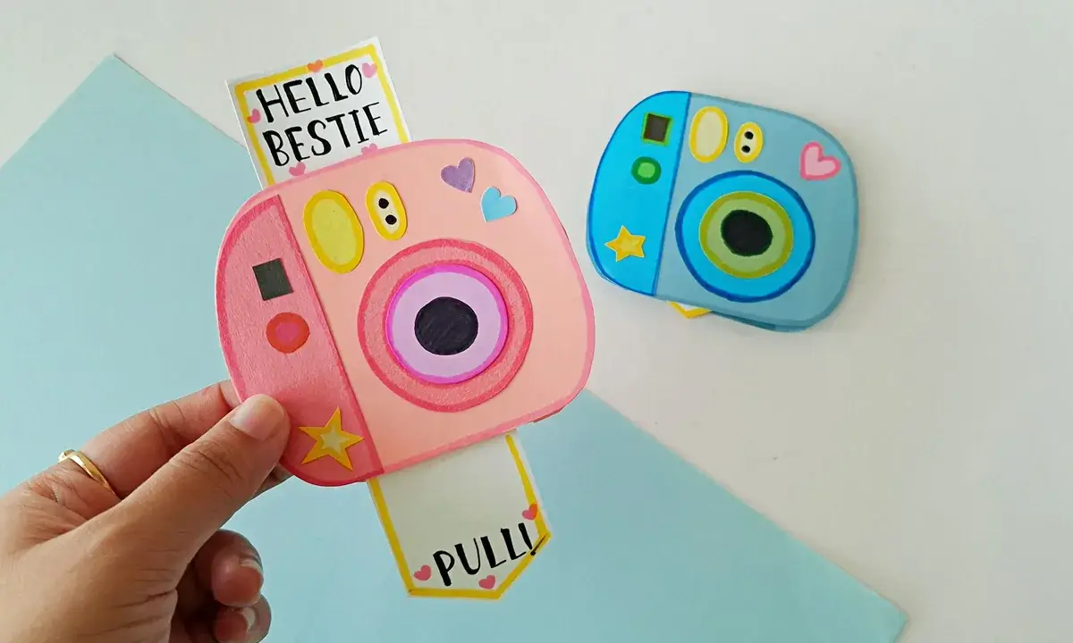 Finished paper polaroid camera cards Two finished paper polaroid camera cards, a pink one pulled open reading Hello Bestie and a blue one