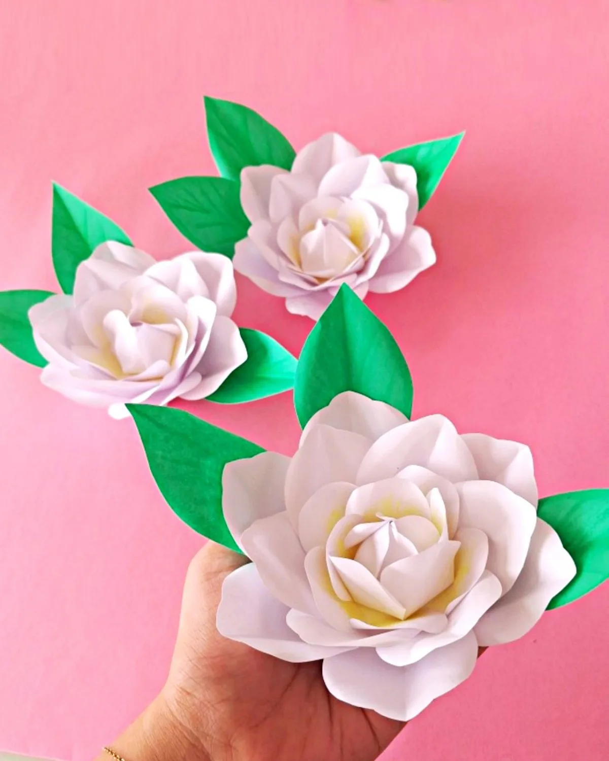 How to Make a Realistic Paper Gardenia Flower 1 Hand holding a finished realistic paper gardenia flower next to two more blooms and paper leaves