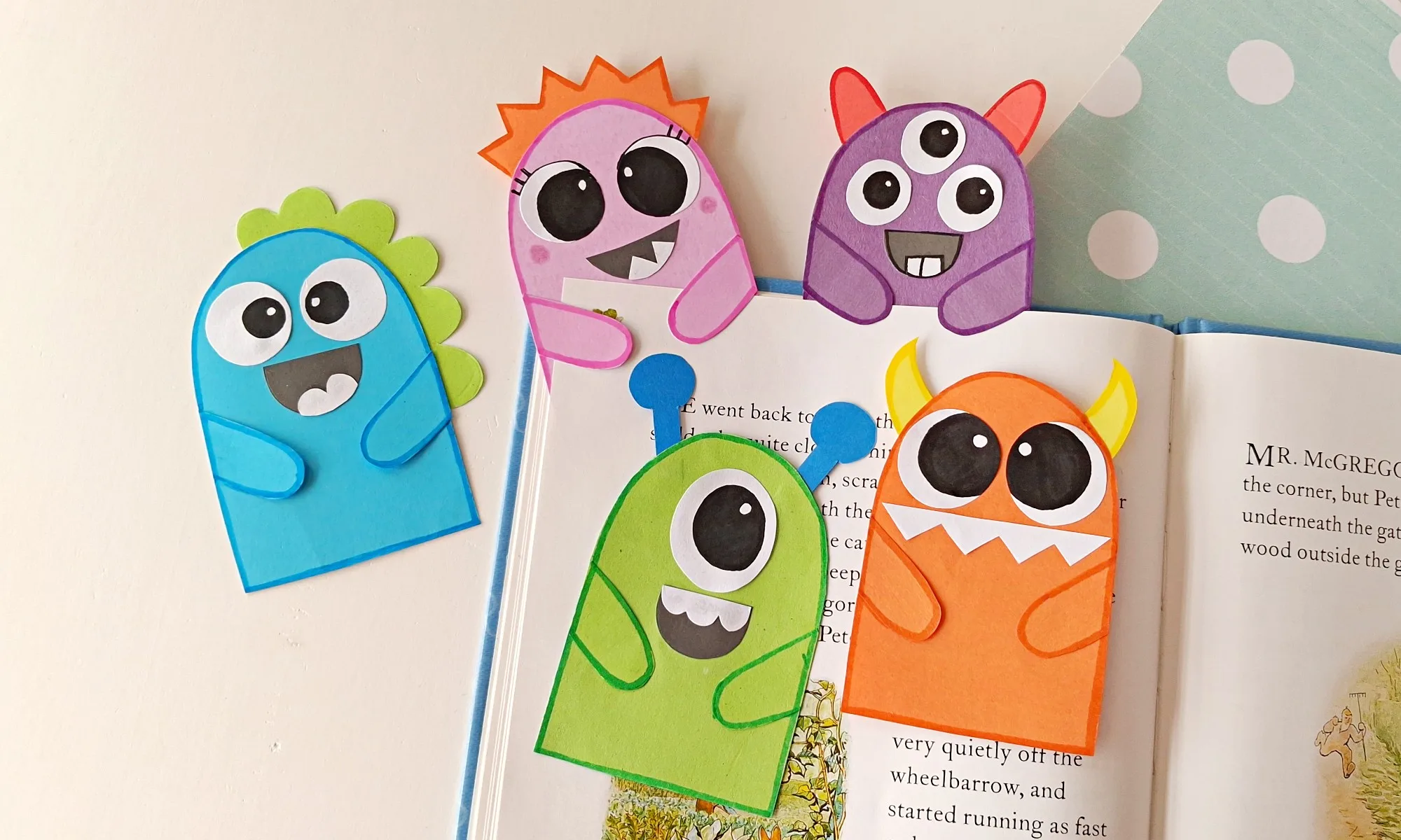 DIY Monster Bookmarks (Easy Paper Craft for Kids) 1 Five colorful paper monster bookmarks peeking over the top of an open book