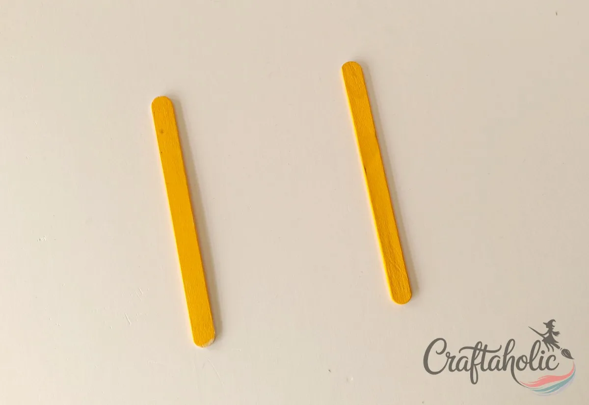 Placing the base popsicle sticks Placing two yellow popsicle sticks as the base for the photo frame