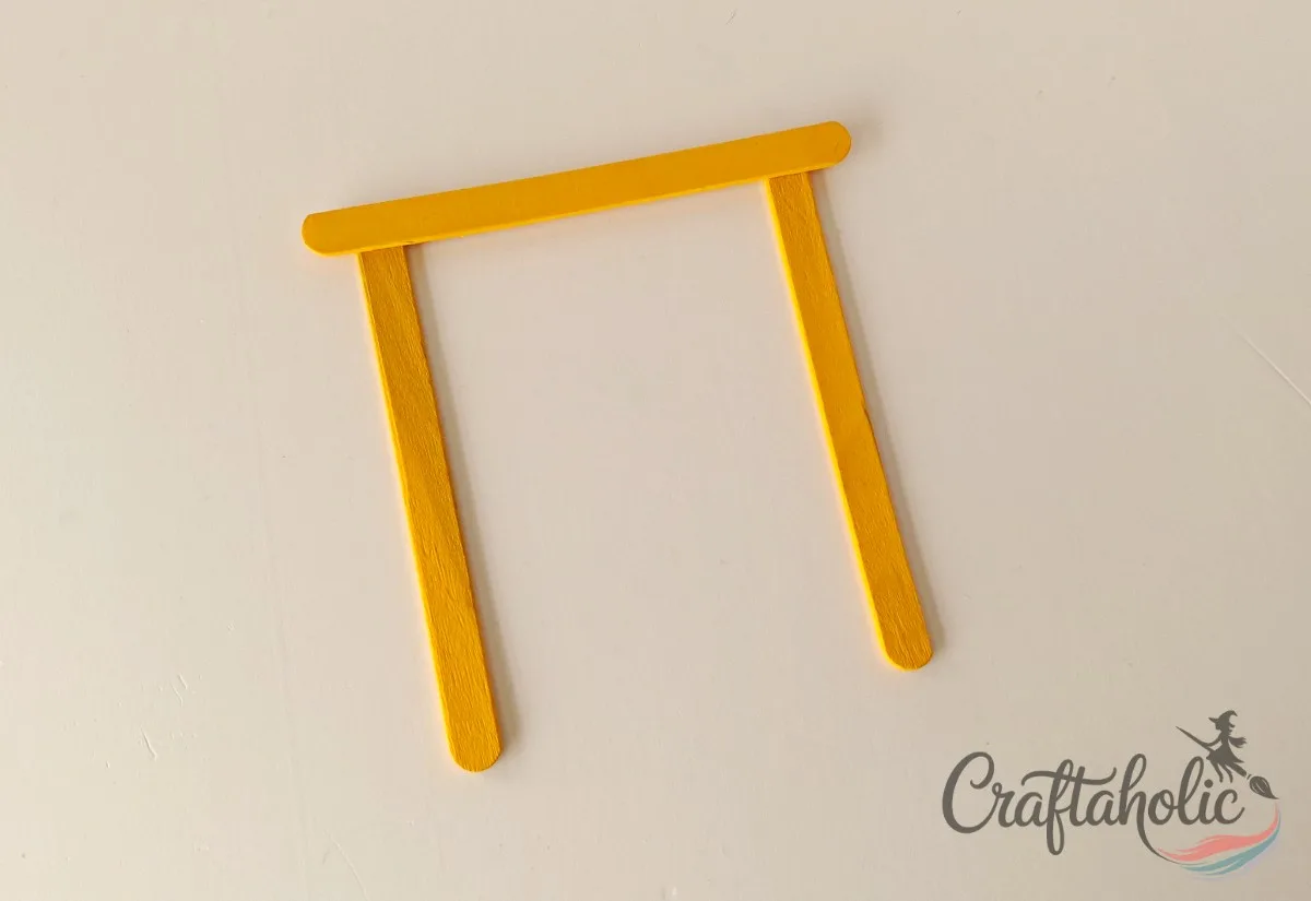 Gluing the top popsicle stick in place Gluing a yellow popsicle stick across the top of the base sticks