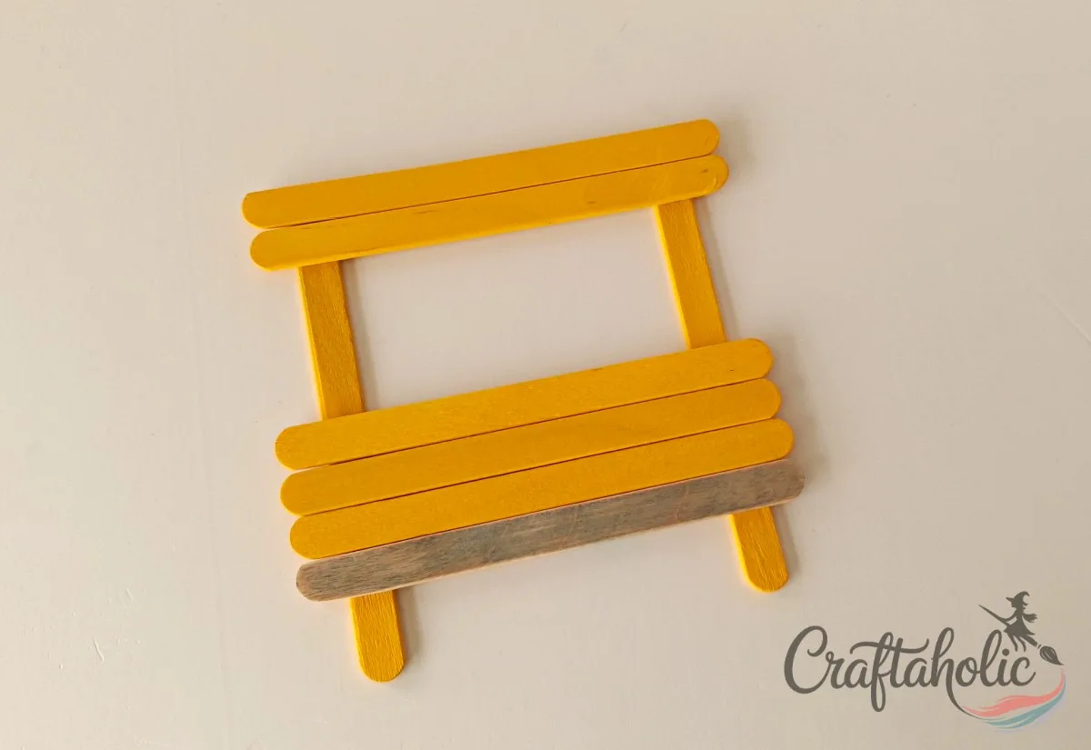 Completing the bus stick pattern Gluing three yellow popsicle sticks above the grey stick to complete the bus shape