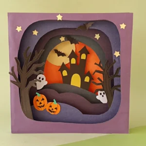 Finished 3D Halloween shadow box made from layered paper art, showing a haunted house under a full moon