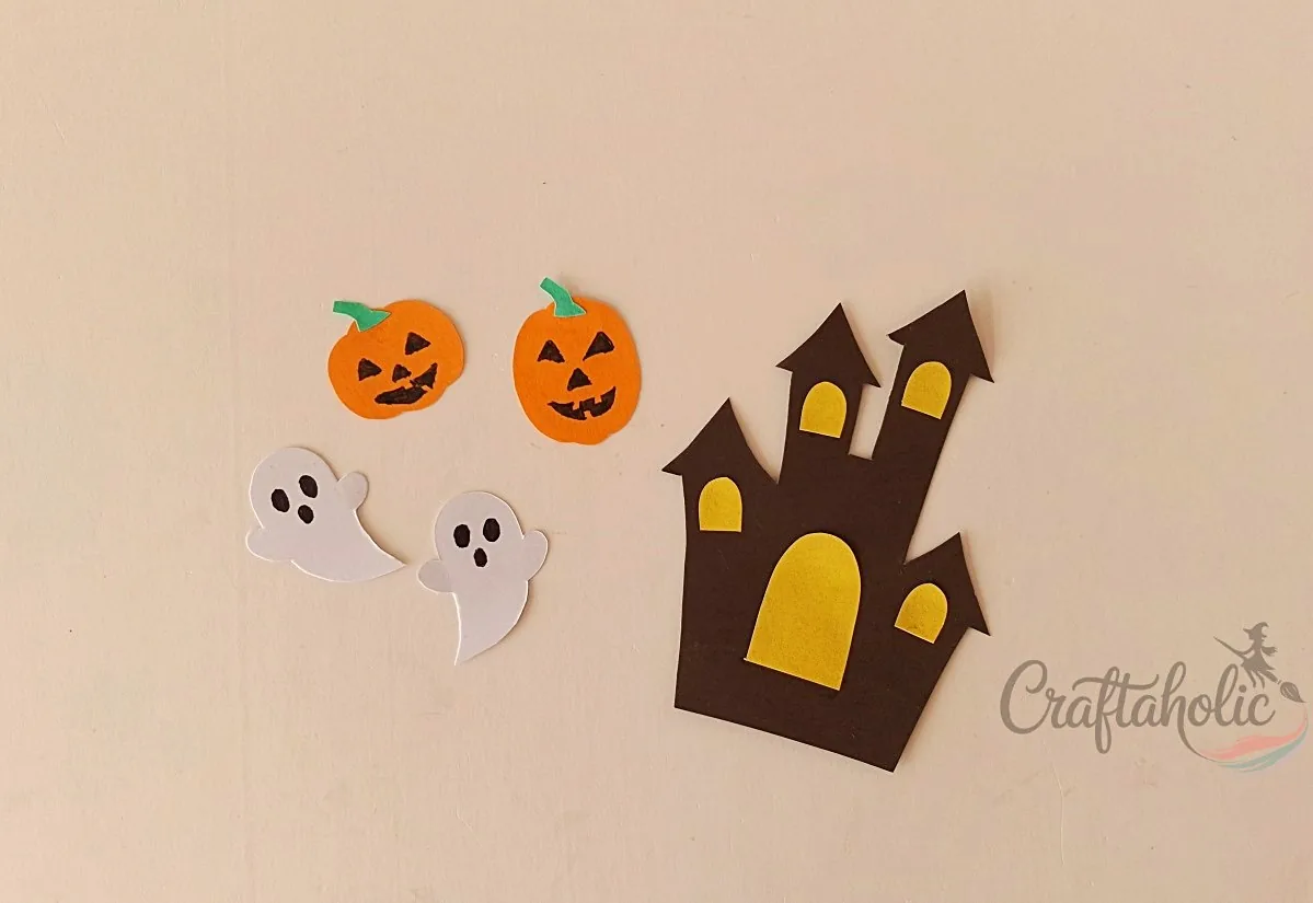 Assembled haunted house and ghosts Paper haunted house with yellow windows and door beside jack-o'-lanterns and ghosts with drawn faces