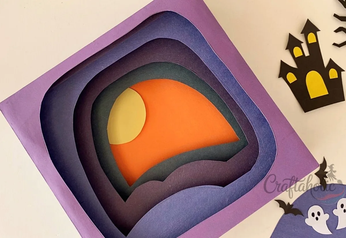 Gluing the moon to the Base/Background Gluing the paper moon onto the orange background of the layered scene