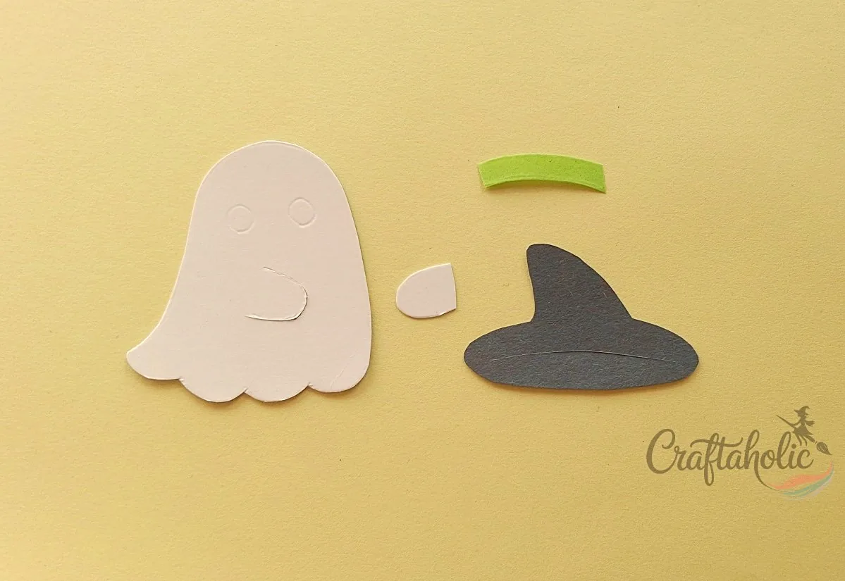 Cutting the hat and arm pieces Hat, hat band, and arm cutouts prepared from craft paper for the ghost lollipop holder
