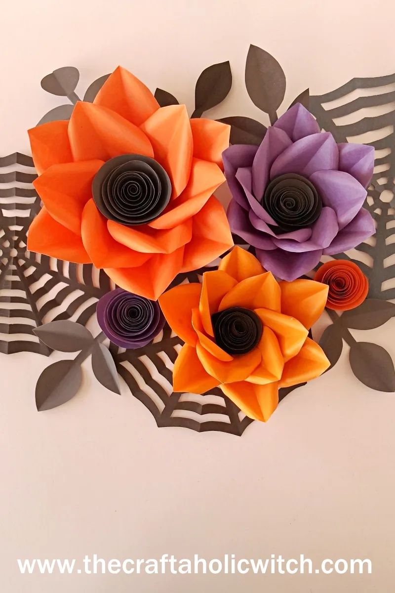 Halloween paper flower wall art with orange and purple flowers over black paper spider webs