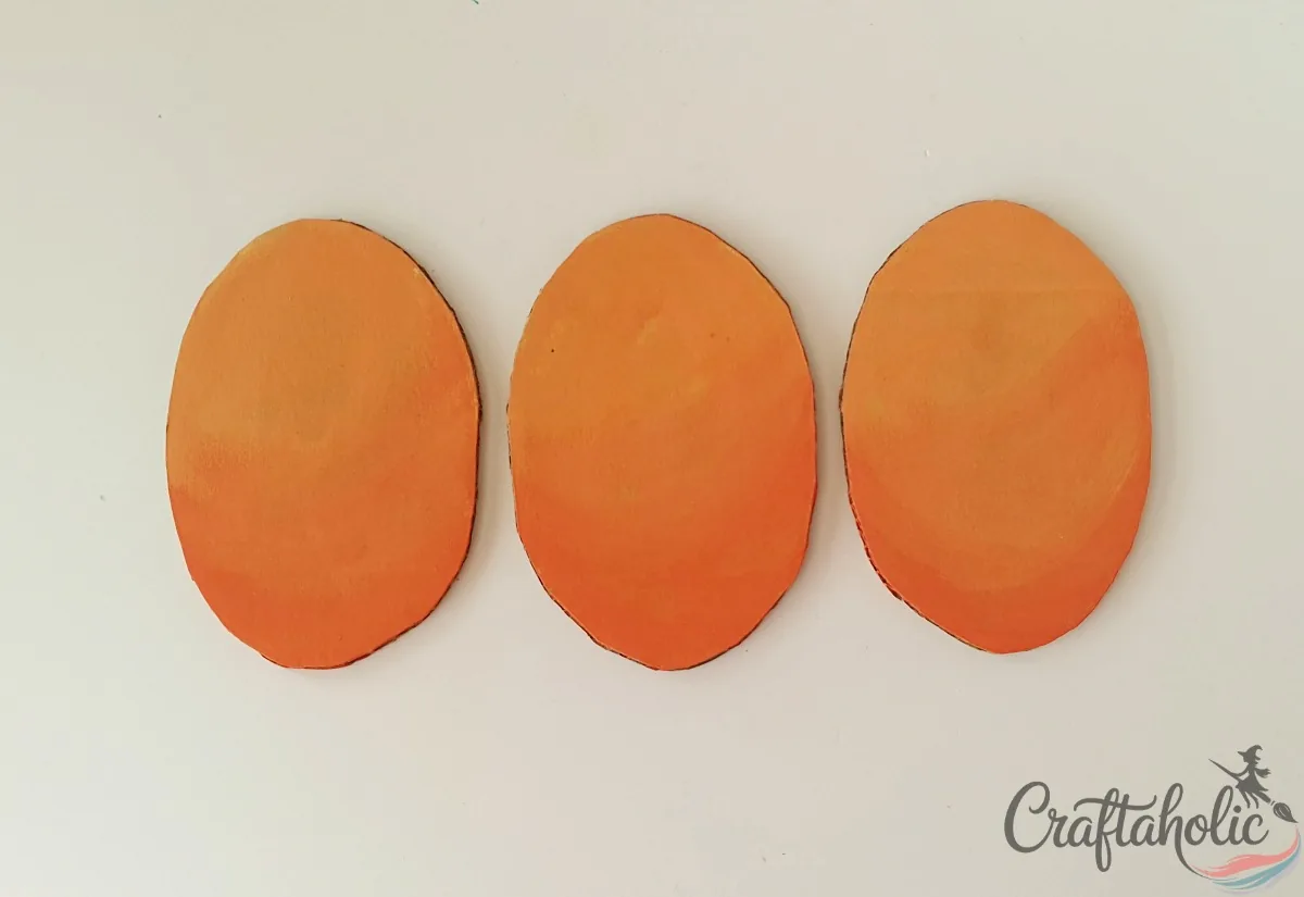 Three cardboard ovals painted in a yellow to orange gradient with acrylic paint