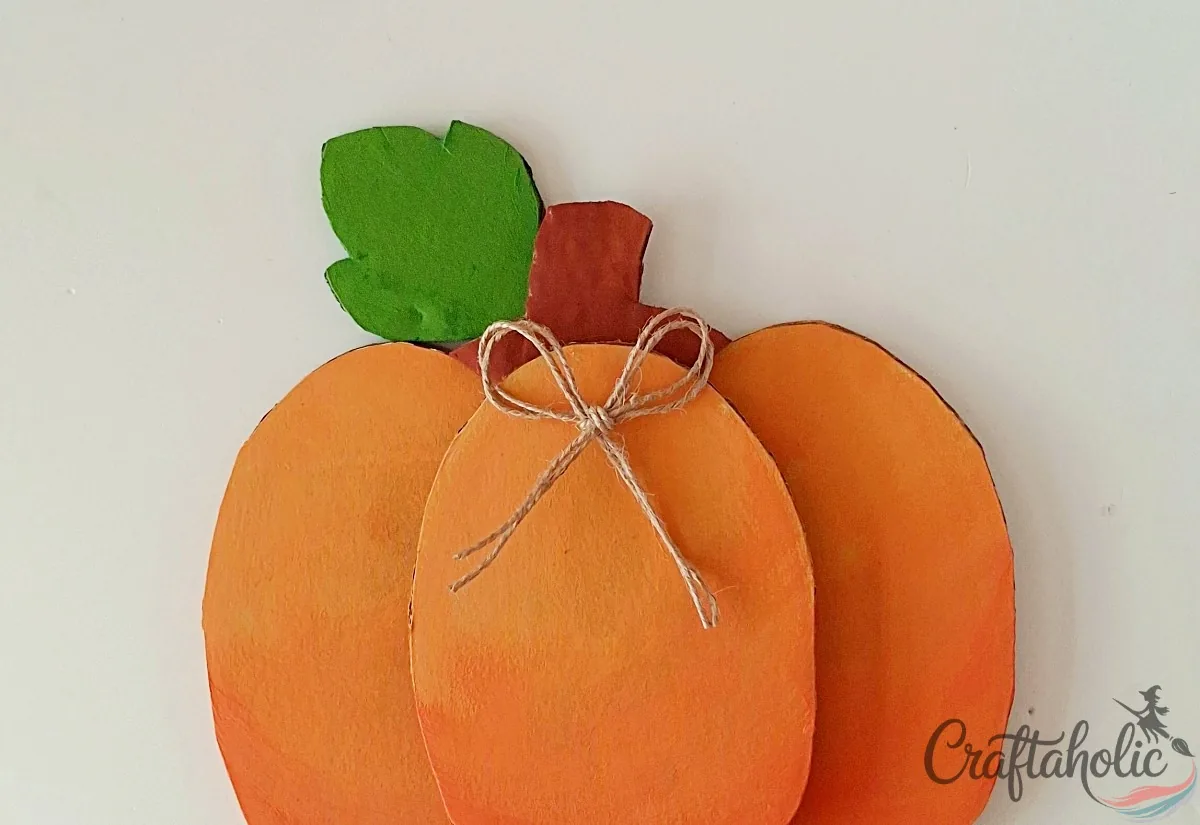 Cardboard pumpkin with a green leaf, a twine bow and gold marker outlines added