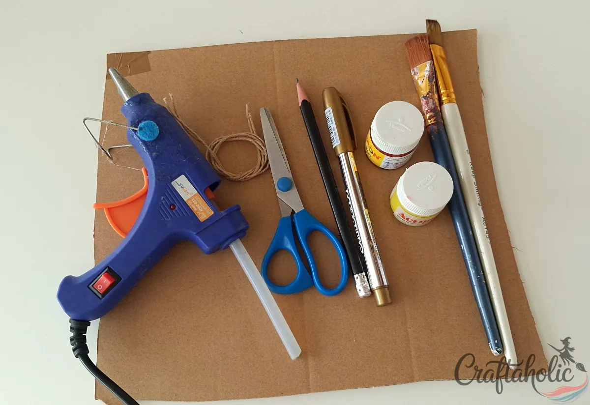 Supplies for a cardboard pumpkin craft: cardboard, hot glue gun, scissors, pencil, paint and twine