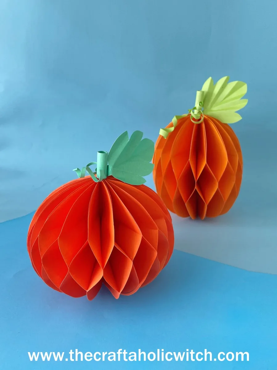 Honeycomb paper pumpkins on blue Tall and short honeycomb paper pumpkins with green leaves and curled vines on a blue background
