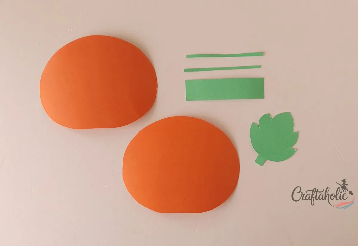 Pumpkin and leaf pieces cut out Cut orange pumpkin pieces beside green stem strips and a green leaf for a honeycomb paper pumpkin