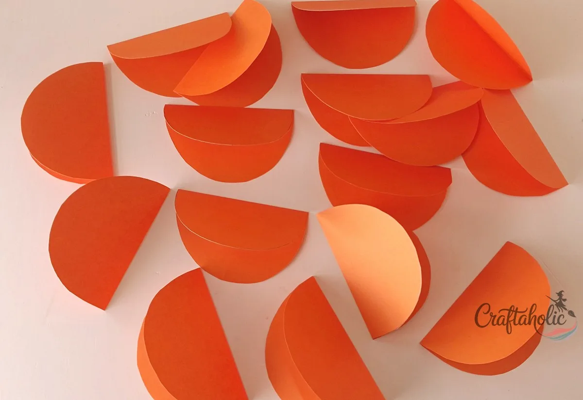 All pieces folded A pile of 18 orange paper pumpkin pieces, each folded in half