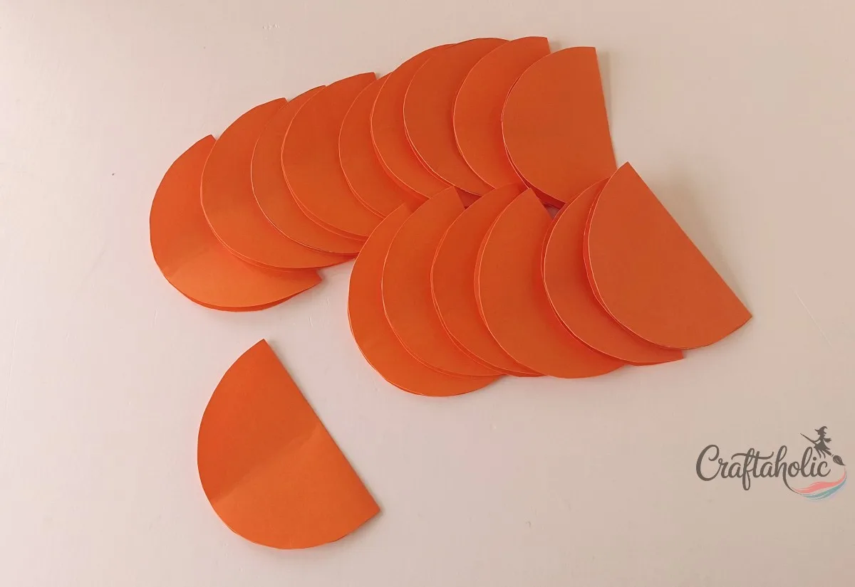 Folding the glued pieces Folding glued orange paper pumpkin pieces shut along the center crease